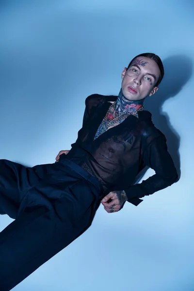 Sexy hombre guapo con tatuajes elegantes tumbado en el suelo y mirando a la cámara, concepto de moda - foto de stock