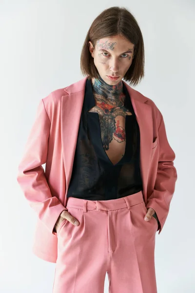 Guapo modelo masculino elegante con tatuajes en chaqueta rosa con las manos en los bolsillos, concepto de moda - foto de stock