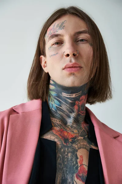 Vertikale Aufnahme eines jungen, stylischen männlichen Modells mit Tätowierungen und Piercings, das in die Kamera schaut, Mode — Stockfoto