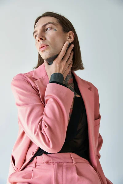 Tiro vertical de joven voguish en chaqueta rosa y pantalones cortos con la mano en el cuello mirando hacia otro lado - foto de stock