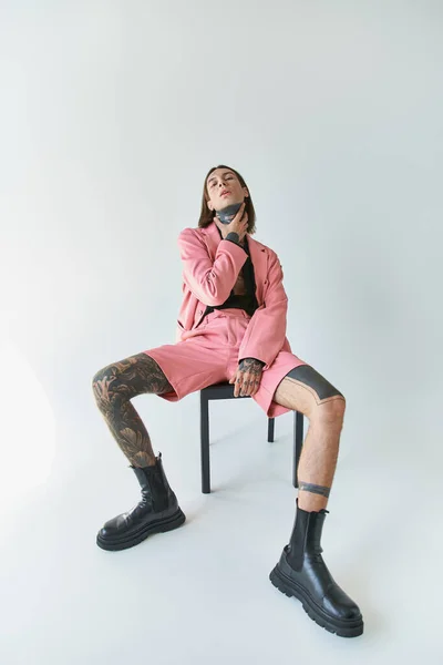 Stilvoller sexy Mann in rosa Blazer und Shorts sitzt auf Stuhl und blickt in die Kamera mit der Hand am Hals — Stockfoto