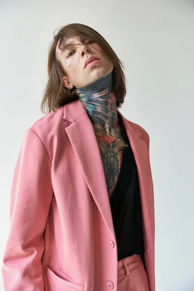 Tiro vertical de joven guapo en chaqueta rosa y camisa transparente mirando a la cámara, la moda - foto de stock