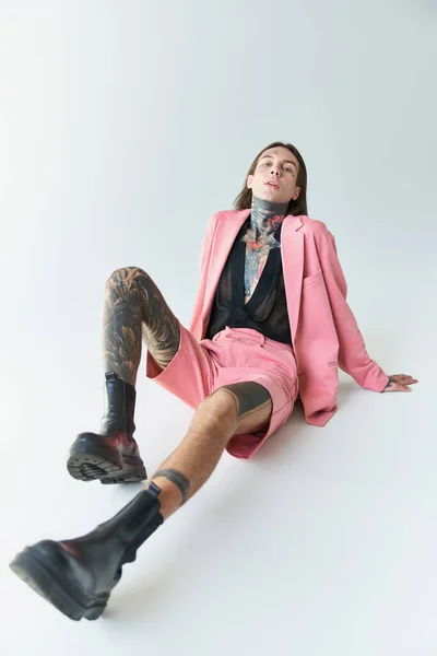 Tiro vertical de un joven guapo en blazer rosa y pantalones cortos sentados en el suelo, concepto de moda - foto de stock
