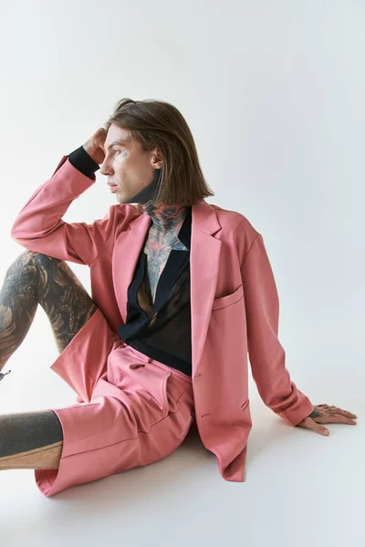 Tiro vertical de hombre sexy guapo con tatuajes sentados en el suelo y mirando hacia otro lado, concepto de moda - foto de stock