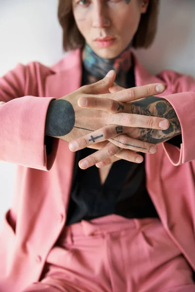 Se centran en las manos con tatuajes de hombre joven y elegante borrosa en traje rosa y negro, concepto de moda - foto de stock