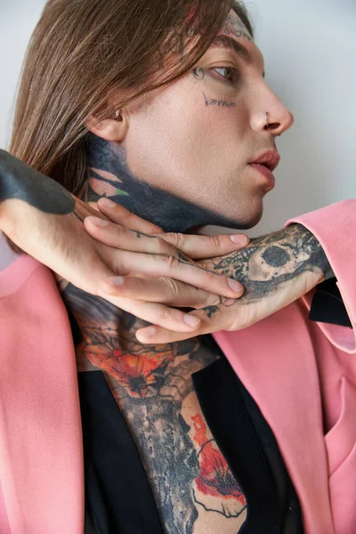 Junger stylischer Mann mit Tätowierungen im rosafarbenen Blazer mit den Händen unterm Kinn, Modekonzept — Stockfoto