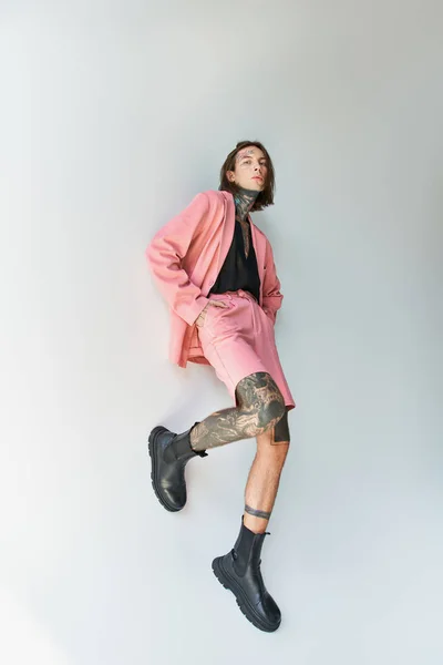 Vertical shot of alluring young man in stylish pink blazer and shorts with leg on wall, fashion — Stock Photo