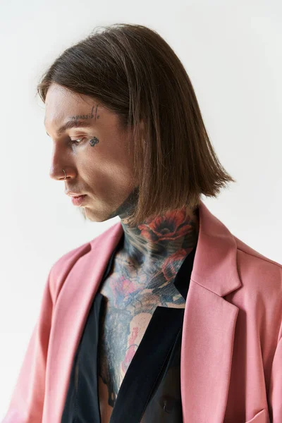 Tiro vertical de hombre guapo con tatuajes elegantes y piercing mirando hacia otro lado, concepto de moda - foto de stock