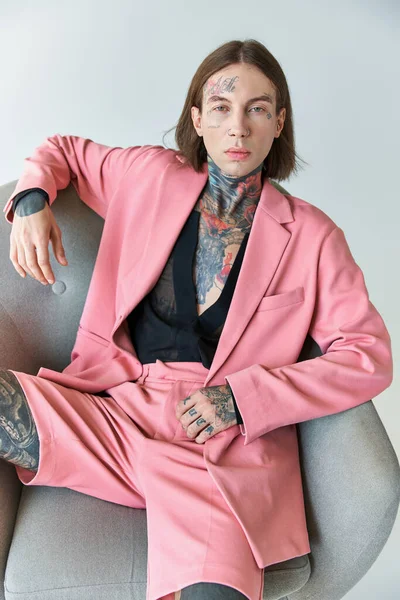 Hombre sexy con estilo en chaqueta rosa y pantalones cortos sentados en la silla mirando a la cámara, concepto de moda - foto de stock