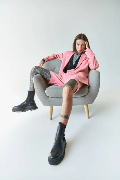 Schöner junger Mann in stylischem rosa Blazer und kurz auf Stuhl sitzend und in die Kamera schauend, Mode — Stockfoto