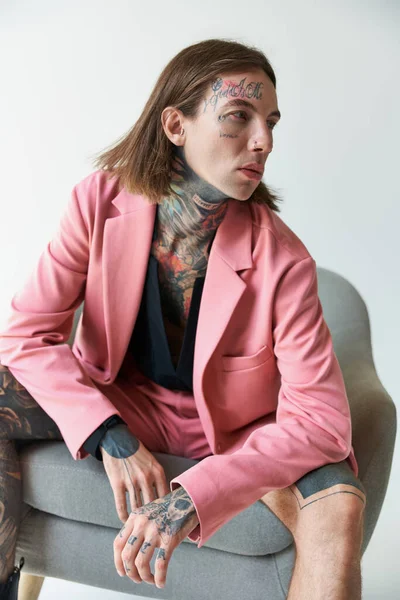 Tiro vertical de seductor joven con tatuajes relajante en la silla y mirando hacia otro lado, concepto de moda - foto de stock