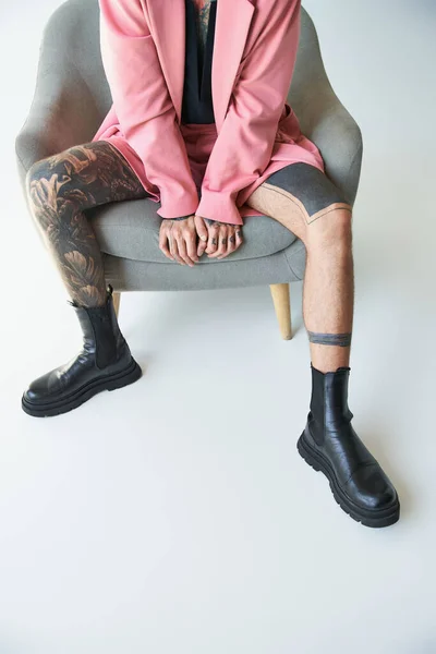 Vista recortada de hombre joven sentado en silla cómoda en chaqueta rosa elegante y pantalones cortos, concepto de moda - foto de stock