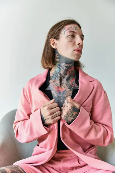 Tiro vertical de seductor joven con tatuajes sentado en silla cómoda mirando hacia otro lado, la moda - foto de stock