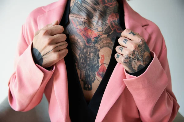 Vue recadrée du jeune homme avec des tatouages avec les mains sur le col de son élégant blazer rose, mode — Photo de stock