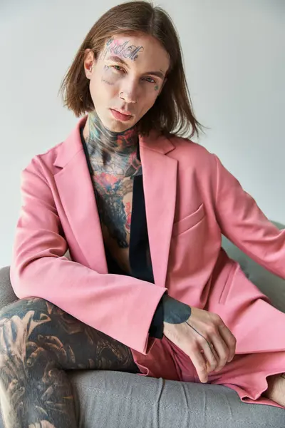 Alluring young man in stylish pink blazer and shorts looking at camera sitting on chair, fashion — Stock Photo