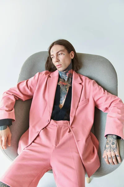 Tiro vertical de hombre sexy de buen aspecto en chaqueta rosa elegante relajante en la silla, concepto de moda - foto de stock
