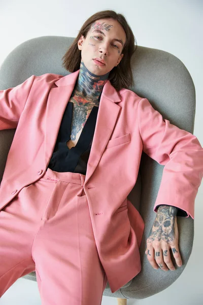 Guapo sexy hombre en traje de moda con tatuajes mirando a la cámara mientras se relaja en la silla, la moda - foto de stock