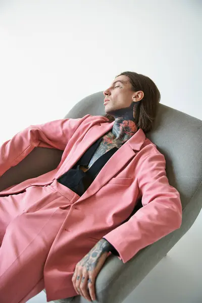 Verführerische stilvolle Mann mit Tätowierungen in voguish Kleidung entspannt in bequemen Stuhl, Modekonzept — Stockfoto