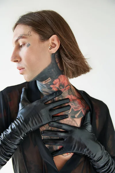 Vertikale Aufnahme eines jungen Mannes mit Tätowierungen und Piercings, der im Profil mit den Händen am Hals posiert, Mode — Stockfoto