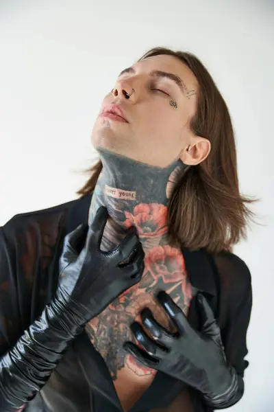Vertical shot of sexy man with tattoos in transparent shirt with hands in leather gloves on neck — Stock Photo