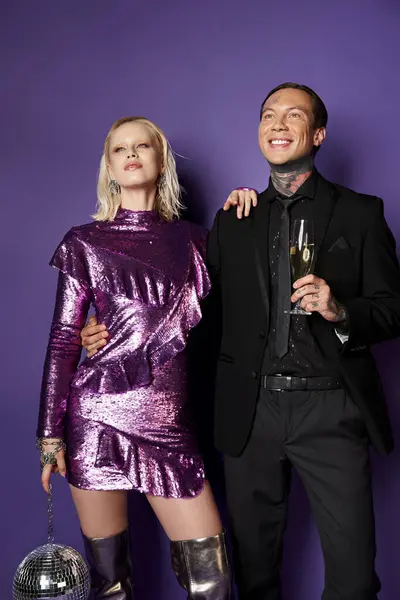 Temps de Noël, couple rêveur en vêtements de fête tenant un verre de champagne et boule de disco sur violet — Photo de stock