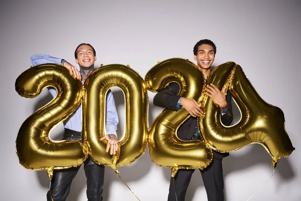 Felici amici maschi interrazziale in possesso di palloncini con 2024 numeri durante la festa, concetto di Capodanno — Foto stock
