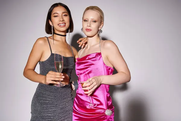 Due donne interrazziale in abiti che tengono bicchieri di champagne sfondo grigio, festa di Capodanno — Foto stock