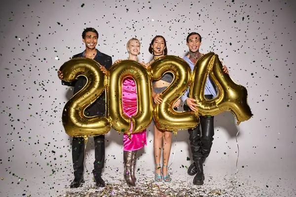 Happy interracial friends holding balloons with 2024 numbers near falling confetti, New Year party — Stock Photo