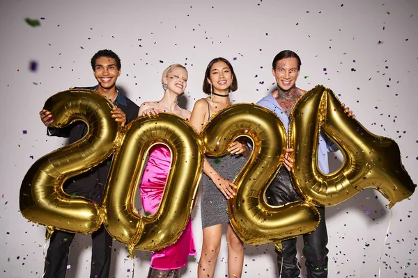 Multiethnic friends holding balloons with 2024 numbers near falling confetti, New Year party fun — Stock Photo