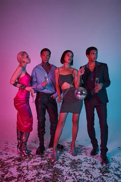 Чотири мультикультурні друзі тримають келихи шампанського та диско-м'яч на фіолетовому рожевому тлі — стокове фото