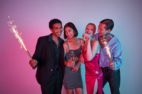 Christmas celebration, radiant multiethnic friends holding sparklers and champagne on purple pink — Stock Photo