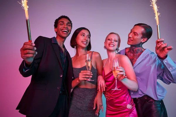New Year party concept, joyous multiethnic friends holding sparklers and champagne on purple pink — Stock Photo