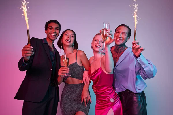 Feliz Navidad y Feliz Año Nuevo, alegres amigos multiétnicos sosteniendo bengalas y champán - foto de stock