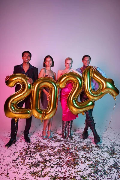 Feliz Navidad y Feliz Año Nuevo, alegres amigos multiétnicos sosteniendo globos con números 2024 - foto de stock