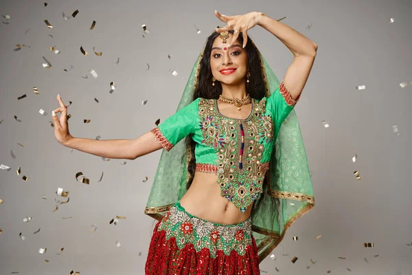 Modelo femenina india atractiva en ropa tradicional posando en movimiento rodeado de confeti - foto de stock