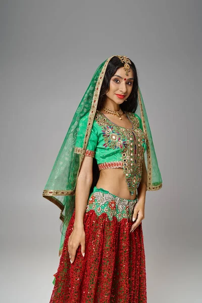 Vertical shot of joyous indian woman in green choli and red skirt with bindi dot looking at camera — Stock Photo