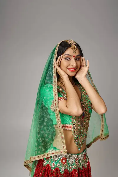 Jolie femme indienne en vêtements nationaux avec bindi et voile regardant caméra, mains près du visage — Photo de stock