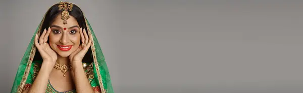 Радостная индийская женщина с бинди точка и зеленая вуаль улыбается в камеру с руками рядом с лицом, баннер — стоковое фото