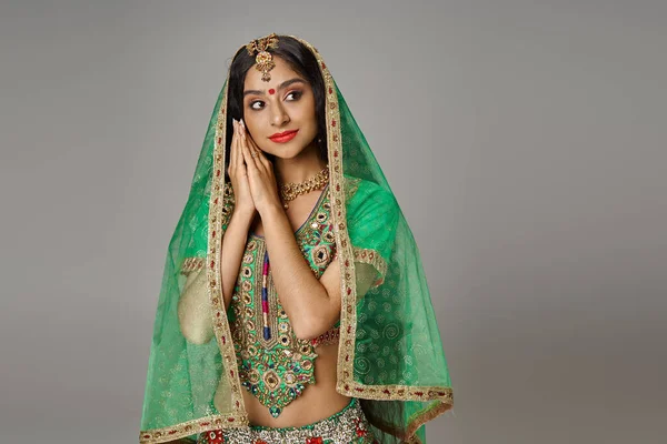 Modelo femenino indio atractivo en traje nacional con velo y bindi posando sobre fondo gris - foto de stock