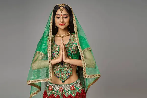 Joyous young indian woman in traditional costume with veil and bindi praying and looking down — Stock Photo