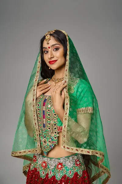 Вертикальний знімок молодої індійської жінки в традиційному одязі та зеленій завісі, що позує на сірому тлі — стокове фото