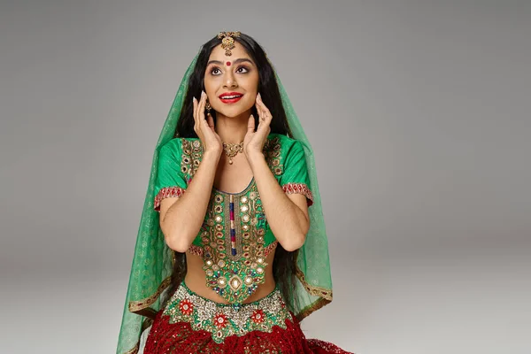 Радостная привлекательная индийская женщина в национальном костюме с точкой бинди, позирующая с руками возле лица — стоковое фото