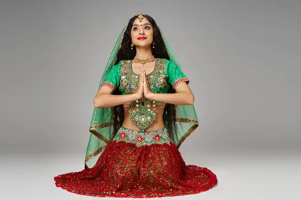 Attractive young indian woman in traditional clothing sitting on knees and praying looking up — Stock Photo