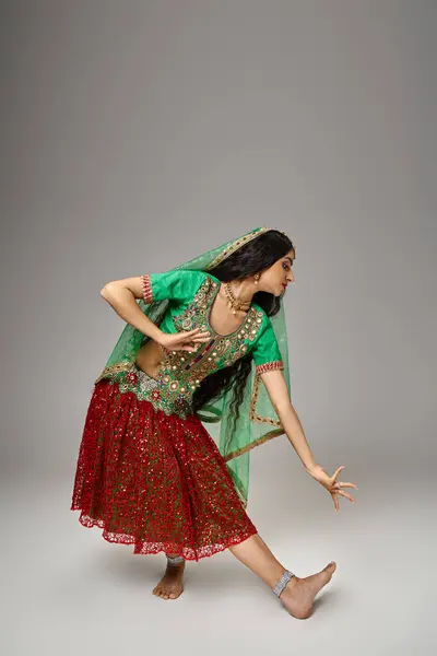Tiro vertical de la atractiva mujer india en choli verde y falda roja gestos mientras baila animado - foto de stock