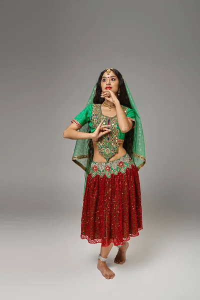 Tiro vertical de la hermosa mujer india en traje nacional con gesto de punto bindi mientras baila - foto de stock
