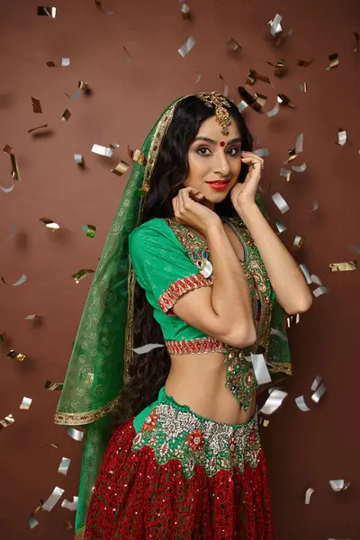 Vertical shot of pretty indian woman in national costume under confetti rain smiling at camera — Stock Photo