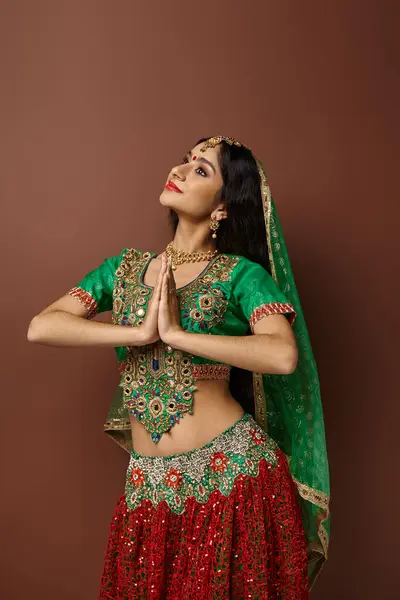 Tiro vertical de mulher indiana com bindi e véu verde mostrando gesto de oração e olhando para longe — Fotografia de Stock
