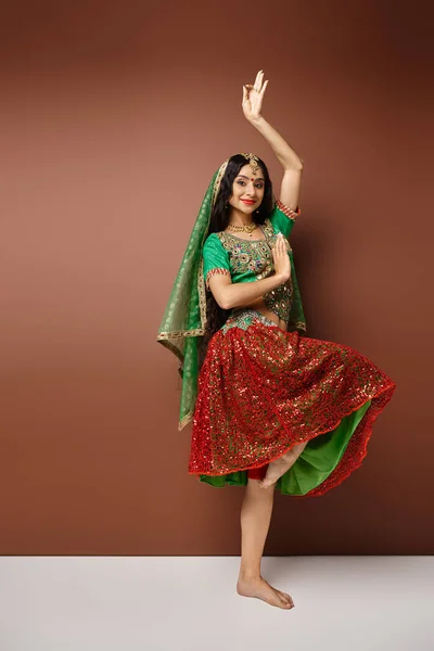 Вертикальный снимок веселой молодой индианки в национальных костюмах, танцующей живо и смотрящей в камеру — стоковое фото