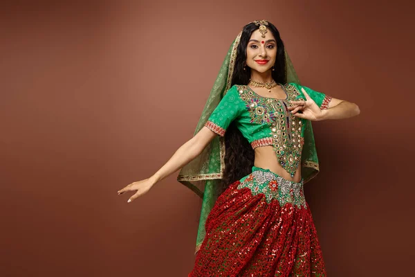 Joyeuse jeune femme indienne en choli vert avec bindi point geste tout en dansant en regardant la caméra — Photo de stock