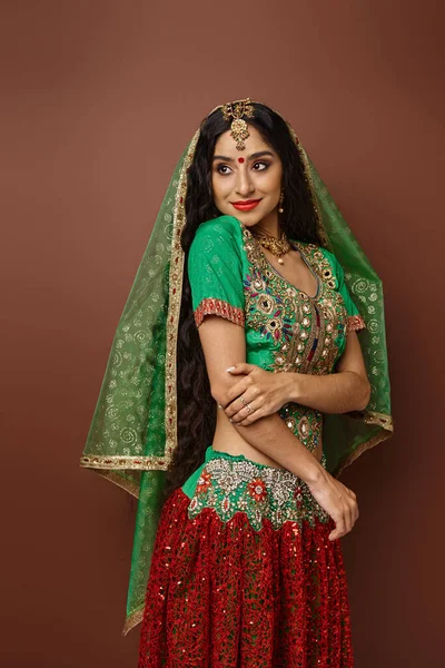Vertikale Aufnahme einer schönen jungen indischen Frau in traditioneller Kleidung, die vor braunem Hintergrund posiert — Stockfoto